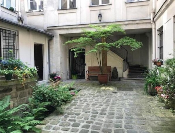 Un patio con sendero adoquinado, banco de madera y plantas en macetas.