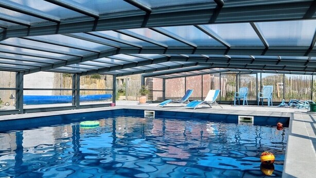 An indoor swimming pool with a glass ceiling, blue lounge chairs, and a view of the outside. - Gîte 7 people -  2 swimming pools (1 with telescopic dome) - The beach on foot (Trégunc)