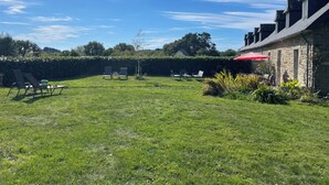 A spacious outdoor area with a stone building, a red umbrella, and several chairs. - Gîte 7 people -  2 swimming pools (1 with telescopic dome) - The beach on foot (Trégunc)