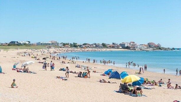 Ein überfüllter Strand mit badenden Personen, Sonnenschirmen und Zelten.