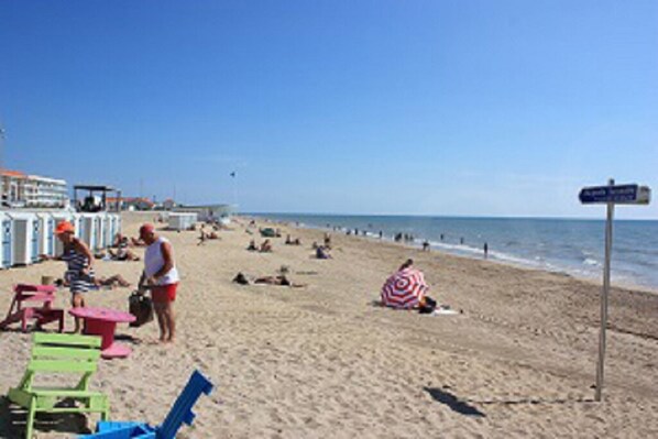 Een strand met mensen die zonnebaden en zwemmen. Er staan strandstoelen en parasols.