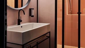 A modern bathroom with a round mirror, a white sink, and a glass-enclosed shower.