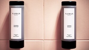 Two NAMAN branded products, an energising shower gel and a vitalising shampoo, displayed on a tiled wall.