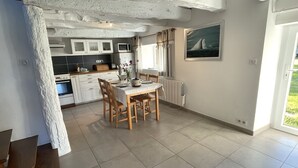 Une cuisine avec des meubles blancs, une table à manger avec des chaises et un tableau accroché au mur.