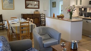 Un saló modern amb un sofà gris, una zona de menjador amb estovatge rayat i una cuina amb armaris blancs i una petita illa.