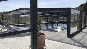 Una estructura de tipus hivernacle amb teulada i parets de vidre, una planta en test i una banca de metall.