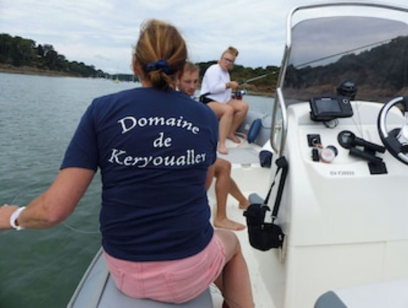Un bote con una persona usando una camiseta que dice "Domaine de Keryoualle" y otra persona pescando.