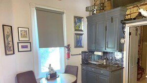 Une cuisine compacte avec un coin repas, comprenant une petite table et deux chaises, une fenêtre avec des stores et un meuble sur lequel est fixé un panneau de signalisation.