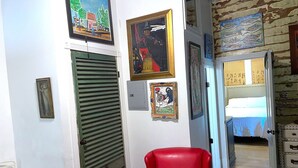Une pièce avec un fauteuil rouge, une porte-volet verte et divers tableaux encadrés accrochés aux murs.