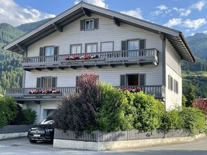 A two-story building with balconies, a car parked in front, and a mountainous backdrop. - Fireplace apartment in Niedernsill with large terrace and garden Pet friendly🐕 (Niedernsill)