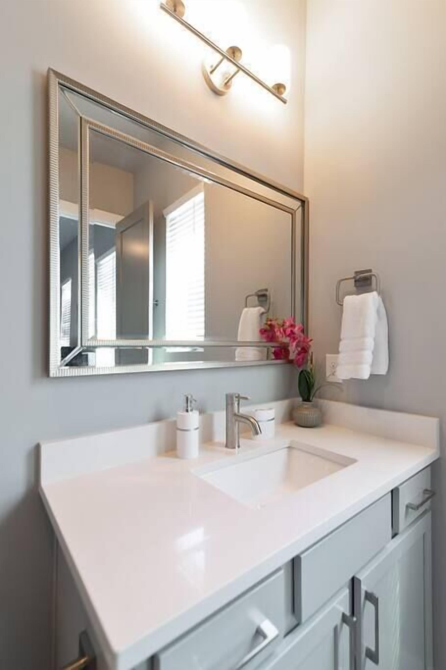A bathroom with a large mirror, a white sink, and a towel rack with white towels.