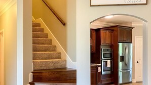 A staircase leading to a kitchen with wooden cabinets and a stainless steel refrigerator. - Beautiful House on the River! Book now for Spring & Summer 2025! (Pangburn)