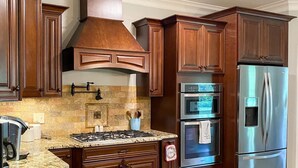 A kitchen with dark wooden cabinets, a stainless steel refrigerator, a built-in oven, and a gas stove. - Beautiful House on the River! Book now for Spring & Summer 2025! (Pangburn)