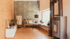 Un salón moderno con suelo de madera, un sofá con cojines, una mesita auxiliar, una lámpara de pie y una estufa de leña.
