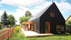 Un edificio moderno de color negro con techo inclinado, una terraza de madera y una puerta de cristal.