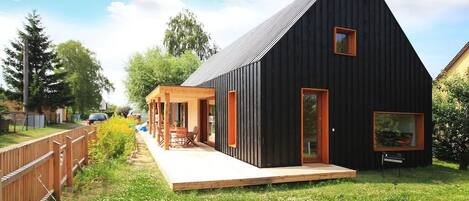 A modern black building with a sloped roof, a wooden deck, and a glass door.