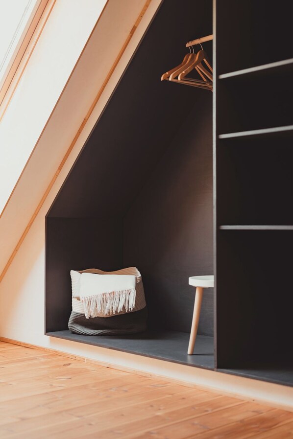 Un dormitorio estilo loft moderno con techo inclinado, armario empotrado, una mesita de noche pequeña y una percha.