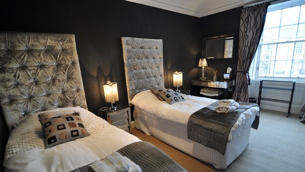 Hotelkamer met twee bedden, elk met een gestoffeerd hoofdeinde, bedlampen, nachtkastjes, een spiegel en een raam met gordijnen.