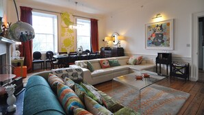 Een ruime woonkamer met een bank, fauteuils, een salontafel en een eethoek met stoelen en een tafel.