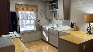 A kitchen with wooden cabinets, a sink, a window with a view of trees, and a stove. - Peaceful Pines Cottage 5 minutes from Old Forge - Lake Access to Lake Tekini (Thendara)