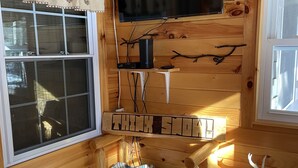 A cozy cabin interior with a mounted TV, a small table with a remote, and a bed with a patterned blanket. - Peaceful Pines Cottage 5 minutes from Old Forge - Lake Access to Lake Tekini (Thendara)