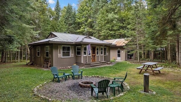A cabin with a metal roof, surrounded by a forest. There are outdoor chairs and a fire pit. - Peaceful Pines Cottage 5 minutes from Old Forge - Lake Access to Lake Tekini (Thendara)