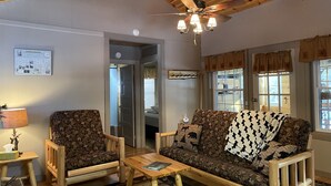 A cozy living room with a wooden ceiling, a ceiling fan, a wooden coffee table, two armchairs, and a sofa with patterned cushions. - Peaceful Pines Cottage 5 minutes from Old Forge - Lake Access to Lake Tekini (Thendara)