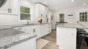 A modern kitchen with white cabinetry, granite countertops, and a central island. - Sleeps 10-Hot Tub-Close to Downtown-Resort Pool (Saugatuck Township)