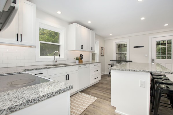 A modern kitchen with white cabinetry, granite countertops, and a central island.