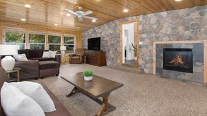 A cozy living room with a stone wall, a fireplace, and a ceiling fan. - Sleeps 10-Hot Tub-Close to Downtown-Resort Pool (Saugatuck Township)