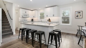 A modern kitchen with white cabinets, a central island with bar stools, and a staircase leading to another level. - Sleeps 10-Hot Tub-Close to Downtown-Resort Pool (Saugatuck Township)