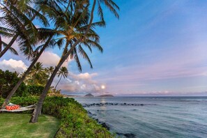 Relax in a serene coastal setting with a hammock nestled among the lush grass overlooking the ocean and distant islands.
