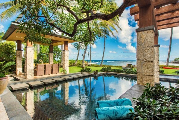 Relax by the ocean with a serene pool surrounded by a deck and pergola, perfect for lounging in tropical surroundings.