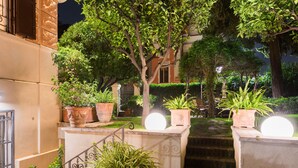 Un espacio exterior bien iluminado con plantas en macetas, una escalera de piedra y la fachada de un edificio.