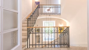 Un interior de varios niveles con una escalera que presenta barandales de metal ornamentados y un pasamanos de madera.