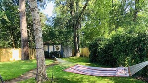 Eine Hängematte in einem Garten mit Holzpforte, Bäumen und einem Weg.