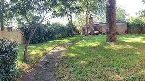 Ein Garten mit einem Ziegelweg, der zu einem Haus führt, umgeben von Bäumen und einem Holzzaun.