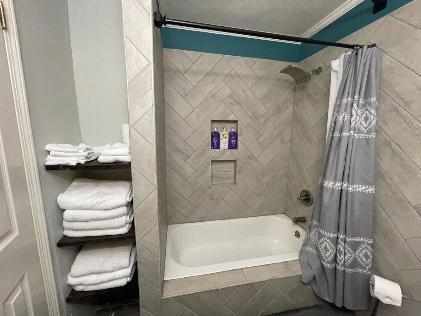A bathroom with a bathtub, a shower curtain, and shelves with folded towels.