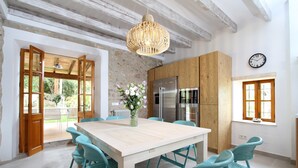 A modern kitchen with a wooden table, teal chairs, a stainless steel refrigerator, and a hanging light fixture. - Can Corme (Pollensa)