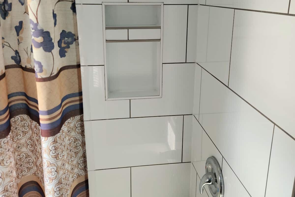 Un baño con paredes de azulejos blancos, ducha e inodoro.