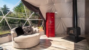 Una habitación acogedora con un sofá redondo color beige, un mueble de almacenaje rojo y un estufa de leña negra.