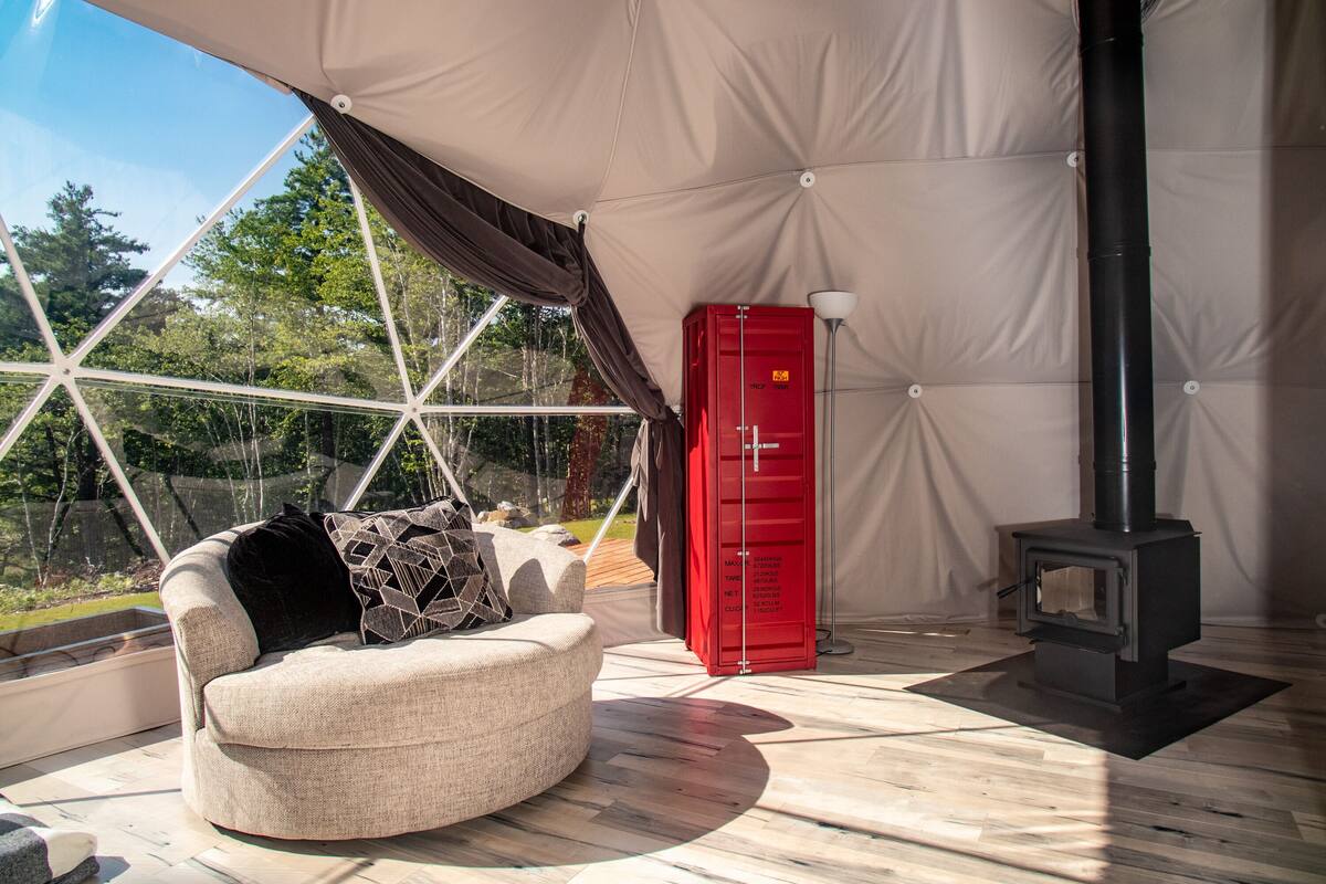 Una habitación acogedora con un sofá redondo color beige, un mueble de almacenaje rojo y un estufa de leña negra.