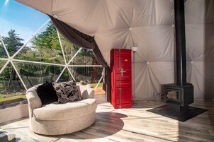 A cozy room with a round beige sofa, a red storage unit, and a black wood stove.