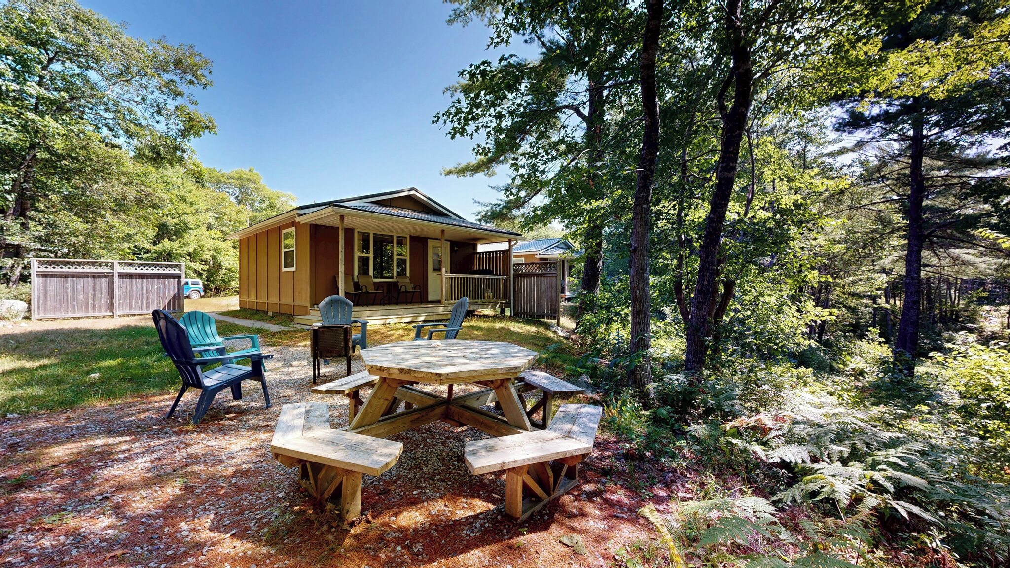 A wooden cabin with a porch, surrounded by trees and a picnic table with chairs.
