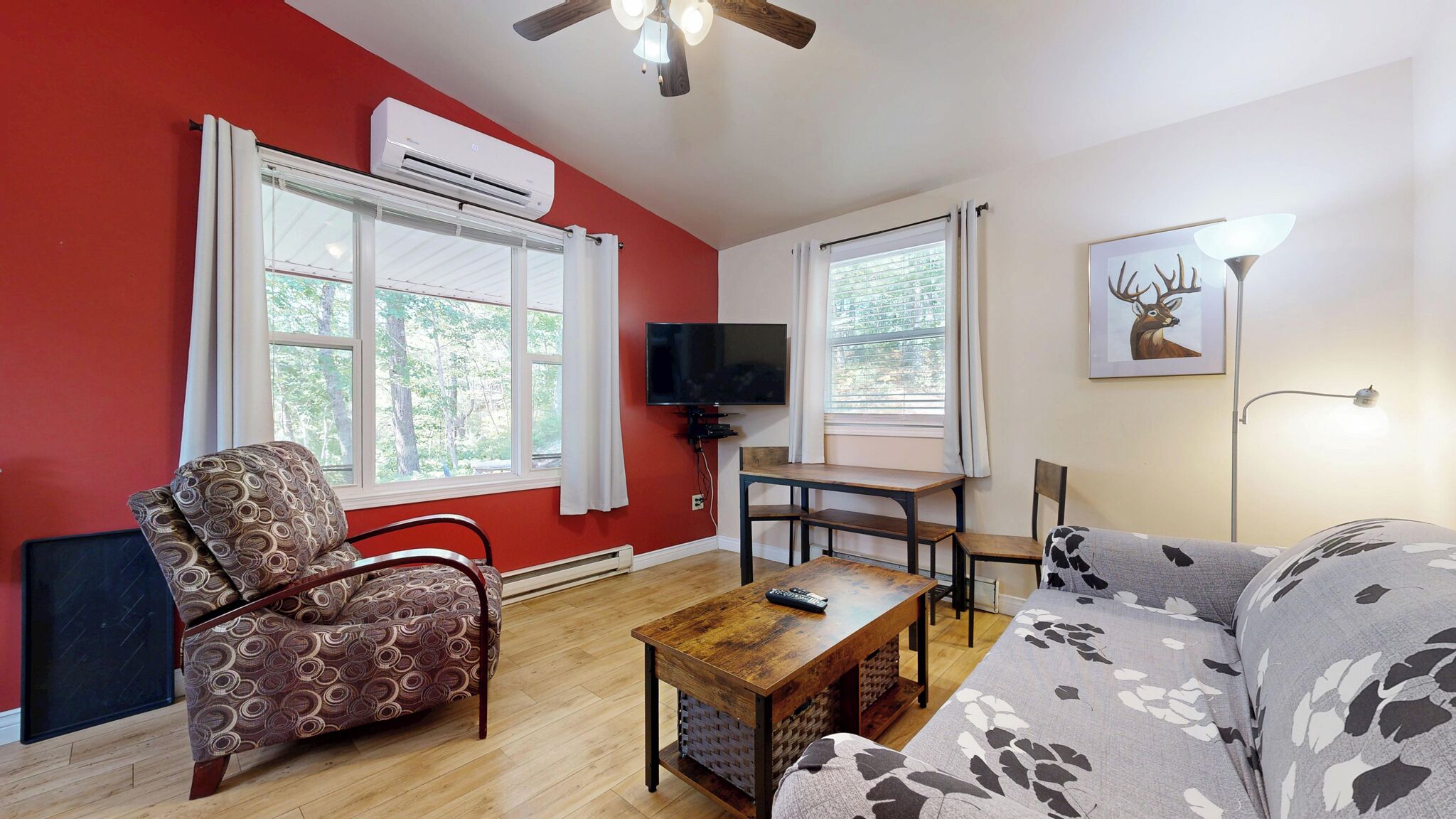 Una sala de estar con pared roja, un sofá, un sillón estampado, una mesa de centro de madera, un televisor y un ventilador de techo.