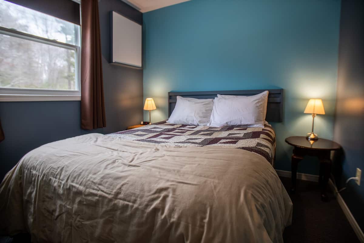 Una cama bien hecha con colcha, dos lámparas de noche y una ventana con cortinas.