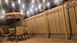An outdoor patio with a table and chairs, string lights, and a wooden fence. - Super Cozy Home Away From Home (Abilene)