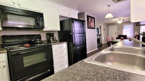 A kitchen with a black stove, microwave, and refrigerator, white cabinets, granite countertops, and a double sink. - Super Cozy Home Away From Home (Abilene)