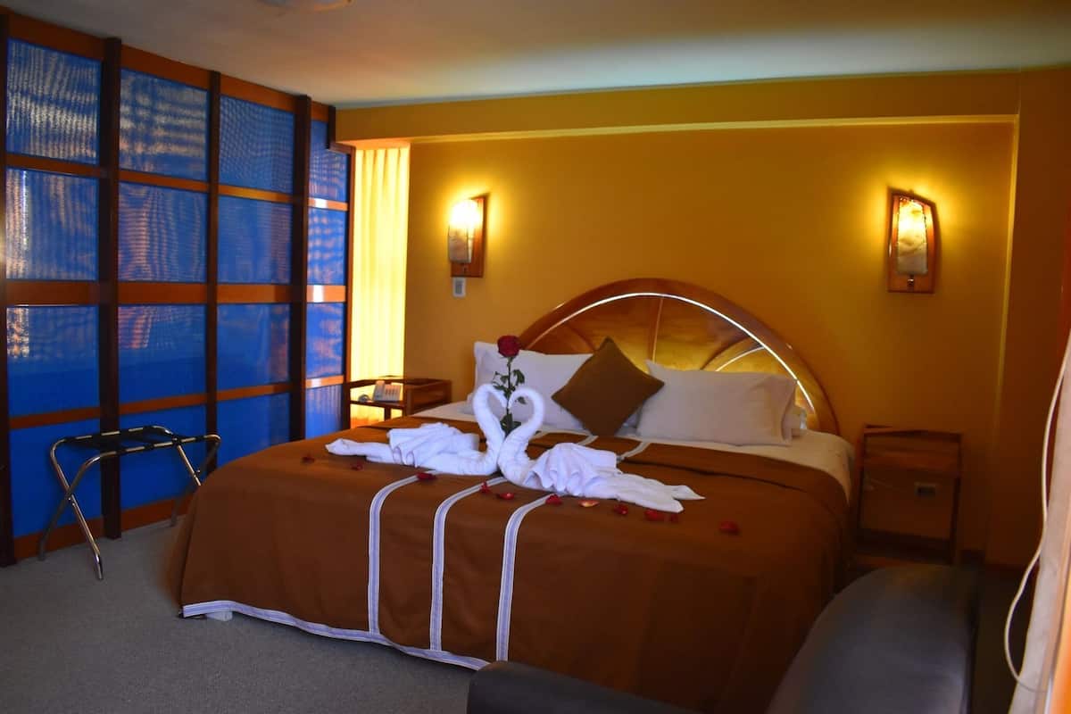 A hotel room with a large bed, two bedside lamps, a window with blinds, and a chair.