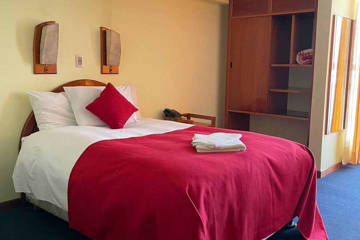 A hotel room with a bed, a wooden wardrobe, a desk, and a window with curtains.